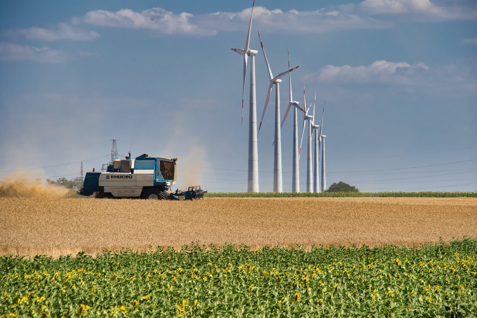 machine harvesting and wind turbine under white clouds and blue sky