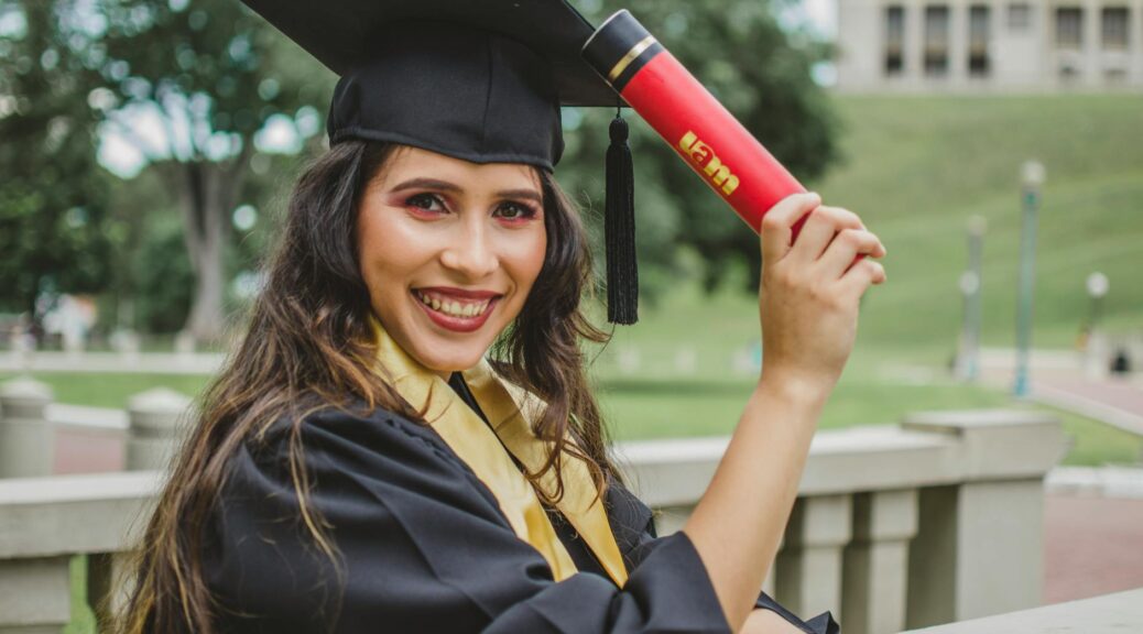 selective focus portrait photo of smiling woman in black academic dress holding diploma posing