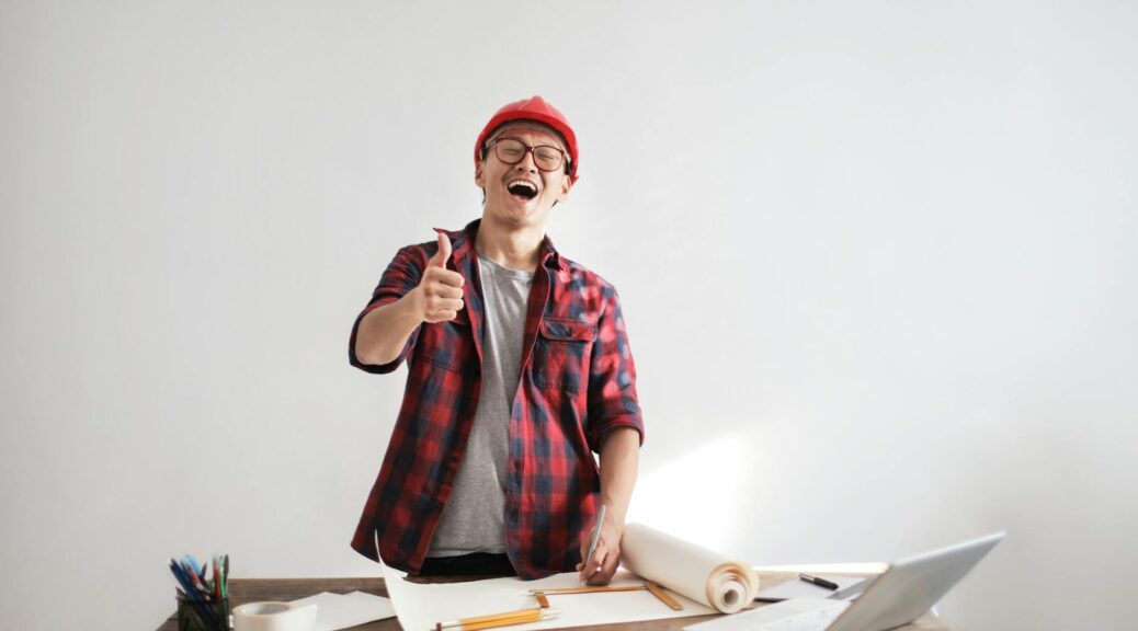 laughing male constructor showing thumb up at working desk