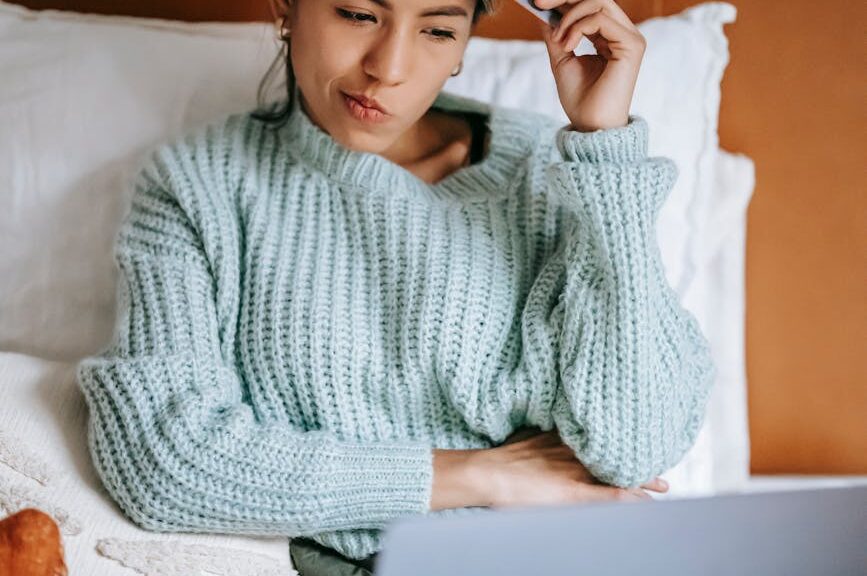 woman with credit card pondering while buying online with laptop