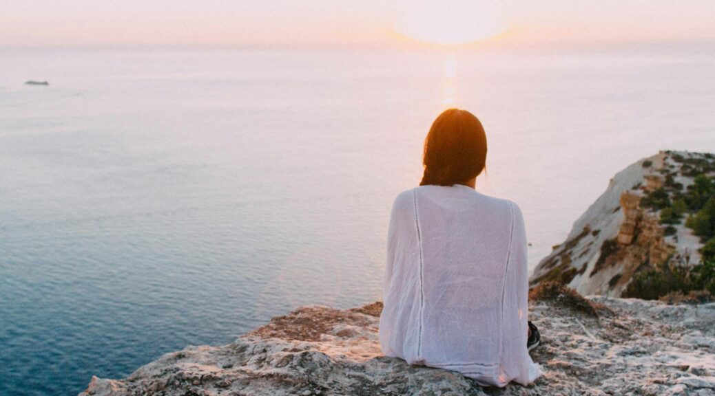 woman sitting on gray rock near body of water