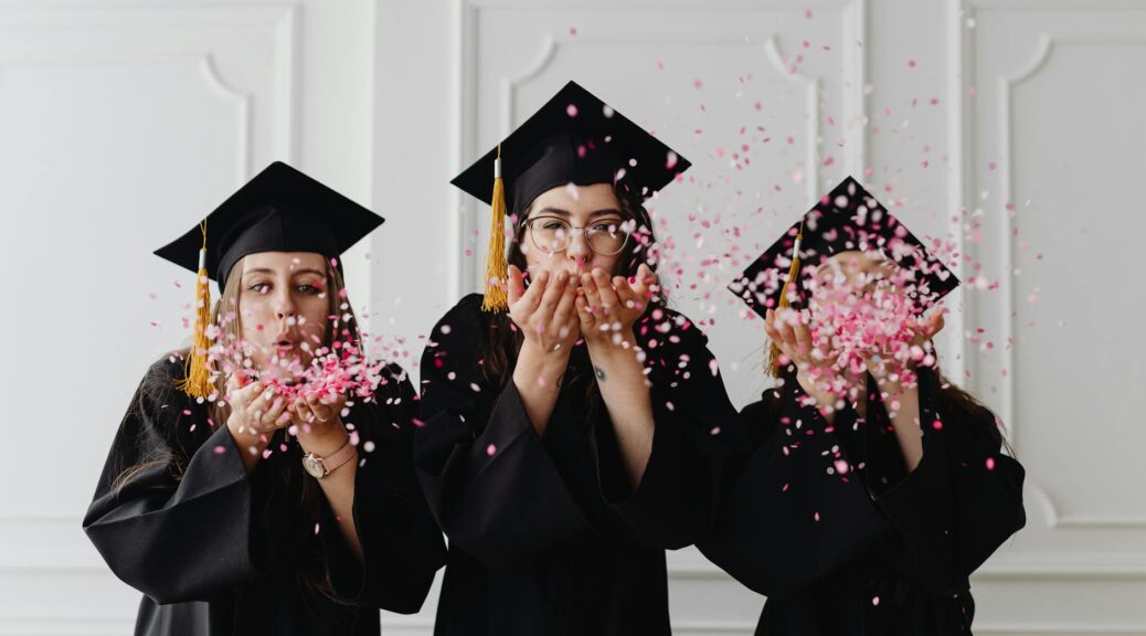 women wearing graduation caps blowing confetti